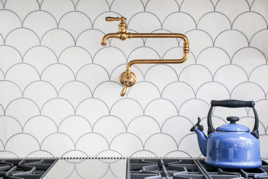 The brass pot-filler behind the stove pairs well with the modern fish-scale backsplash.