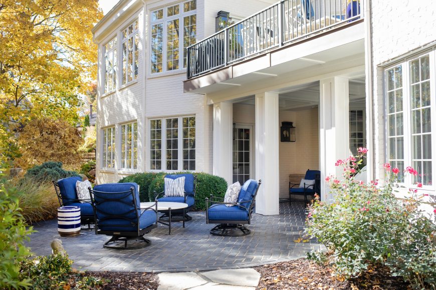 The lower-level patio incorporates the same blue-and- white palette as the rest of the home. The black iron chairs provide a little contrast with the gray stone pavers, while the pillows add fun punches of pattern.