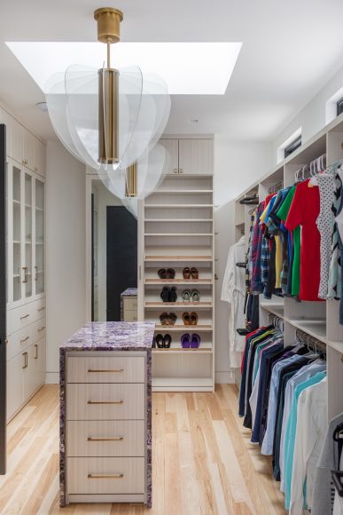 The closet off the home’s primary bedroom contains numerous options for storing clothing, shoes, jewelry and more. The island is topped with purple quartz and underlit — and more light pours in from a skylight.