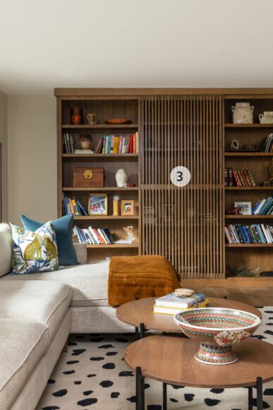 3. In the living room, the homeowner had the custom walnut bookcase built with a sliding, slatted component to hide the TV. “For [the homeowner], it was about keeping [the living room] layered, eclectic and textured, as well as feminine and fun,” says Goeser.  