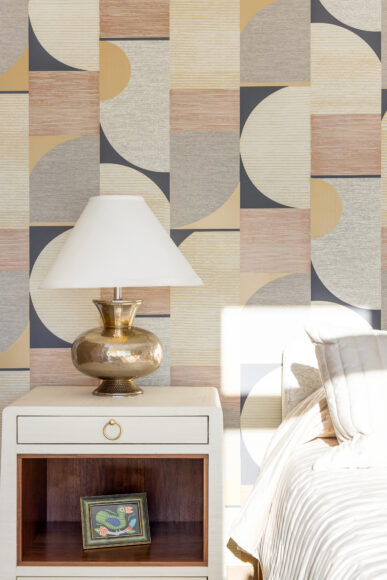 The guest suite’s night table is finished with lacquered grasscloth. Gold is woven in as an accent throughout the home, including in the lamps and furniture hardware in the guest room. Geometric shapes in the guest suite’s wallpaper are eye-catching, yet their earthy tones soothe.