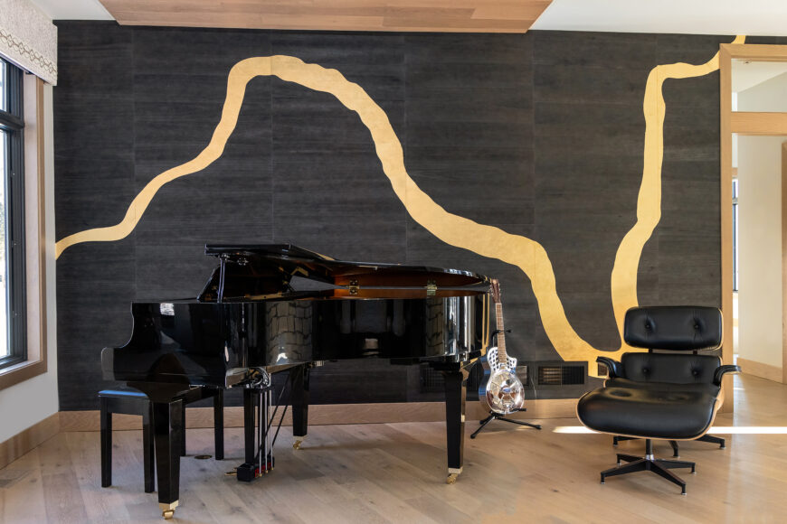 A ribbon of gold metallic leaf rises and falls against an ebony backdrop, showcasing the baby grand piano.