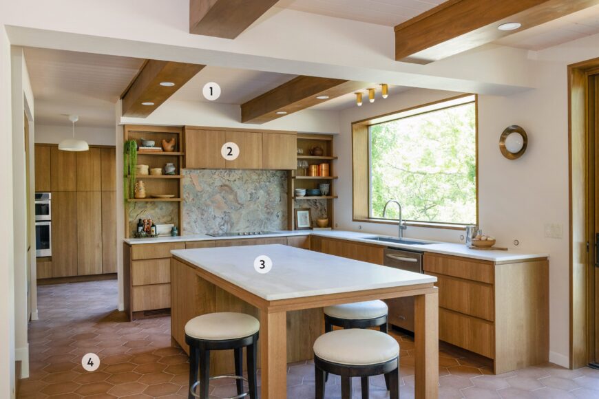 1. The home's original tongue-and-groove ceiling doubles as structural support for the second floor, so Schultz and her team incorporated the kitchen’s can lighting into the beams. The bonus is that it looks stylishly integrated. 
2. Sans hardware, the rift-sawn white oak cabinets with integrated finger pulls have a minimalist, yet stylish, appearance. Floating shelves also add visual interest. 
3. To balance the wood tones, the kitchen island is topped in with a creamy marble countertop to brighten the space. The stools can easily be tucked underneath to save space. 
4. Makoto’s hexagon matte porcelain tile in umi terracotta was chosen for the flooring and its warm, earthy tones ground the kitchen, while the pattern adds a timeless touch of interest.