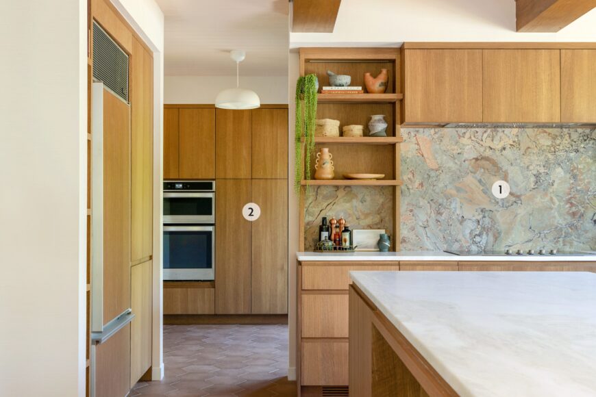 1. According to Schultz, the show-stopping marbled backsplash — a mix of rose, oxblood and cream — was the design centerpiece for the kitchen. “We used it behind the range and beneath the shelves as a focal point,” she explains. The striking surface beautifully ties together the kitchen’s mix of materials, including warm wood, mixed metals and the earthy floor tiles. 
2. Tucked behind the kitchen, the pantry adds both function and style with rift-sawn white oak cabinetry that offers generous storage. It also houses the integrated oven and microwave which keeps the kitchen free of visual clutter while also providing extra space for food prep and cleanup.