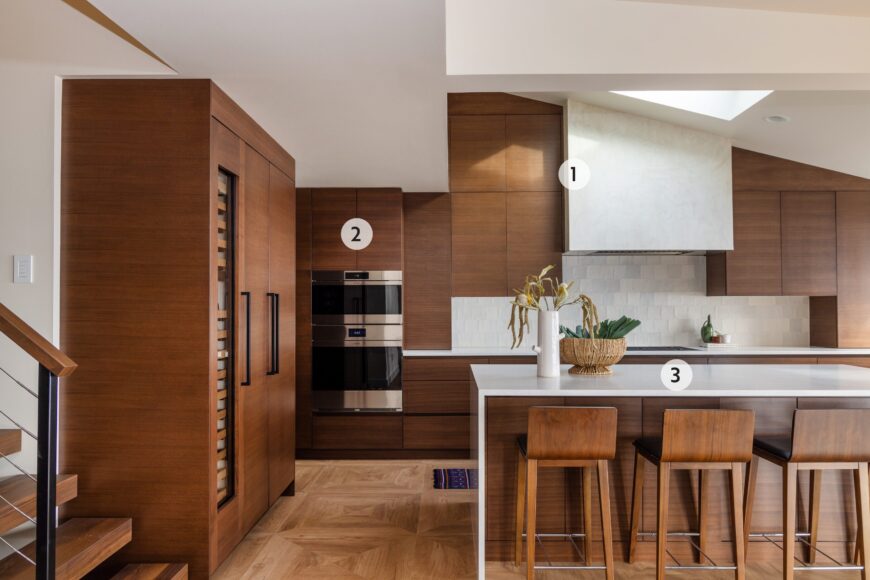 1. The smooth, hand-troweled warm ivory plaster range hood (with a protective finish) was custom-made by Fiddlehammer, a Milwaukee furniture company. 
2. The Plato cabinetry was chosen and installed in collaboration with the Kitchen Ideas Center. The horizontal quarter-sawn walnut shows off the natural wood grain and the smooth fronts keep the design simple, yet seamless. 
3. A waterfall-edge island (topped with Cambria Delgatie quartz) provides a spot for a quick meal. The flooring is actually ceramic, designed to mimic wood (Porcelanosa Heritage Cognac), and is from Flooring Designs.