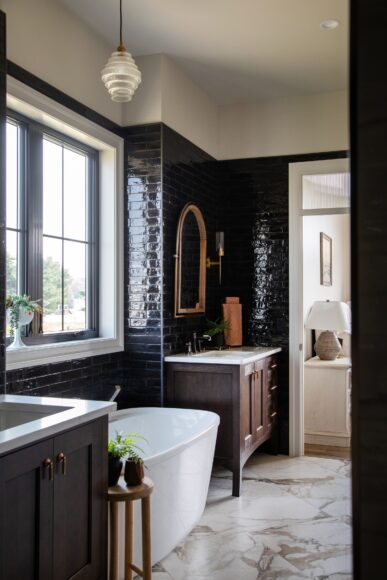 The primary bathroom features deep chocolate wall tile, Kohler fixtures and two furniture-like vanities. “You feel the grandness when you walk in here, but that dark tile … makes the space feel cozy,” says Tonia.